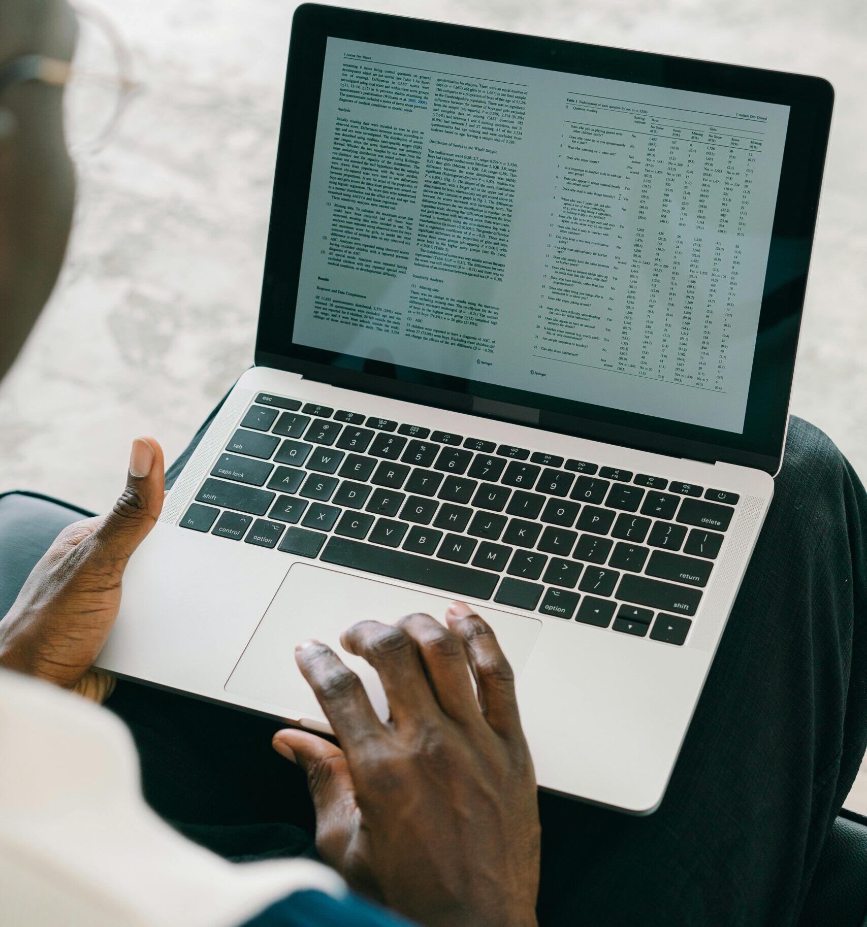 Close-up of a person using a laptop with spreadsheets and text on the screen.